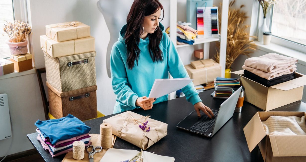Mujer trabajando en su tienda en línea desde casa, revisando pedidos y gestionando inventario de ropa y accesorios